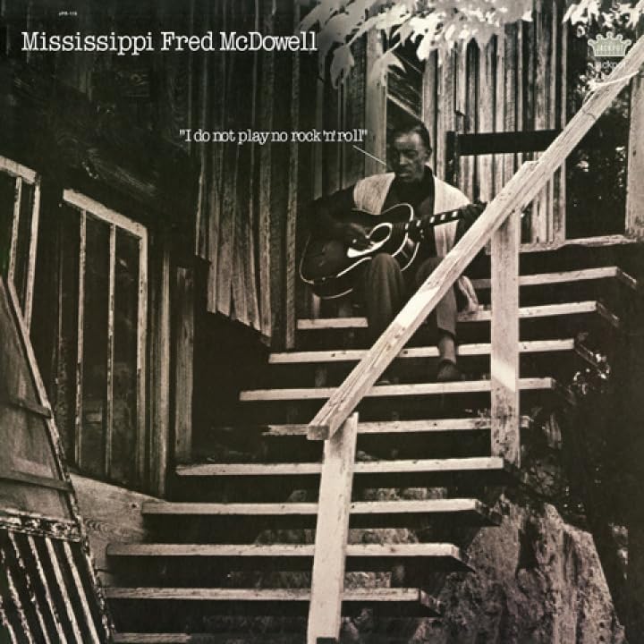 Mississippi Fred McDowell seated on stairs with an acoustic guitar.