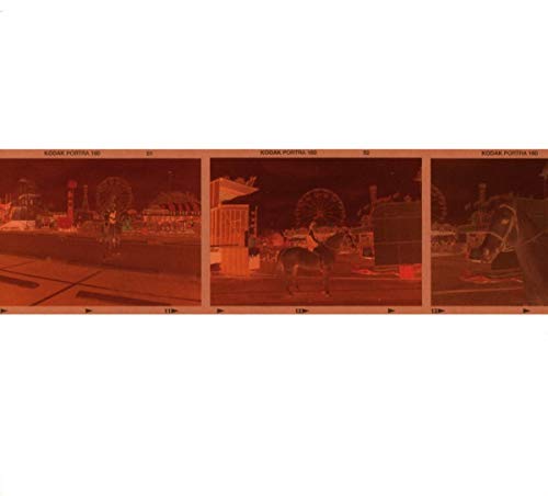 The image shows a red-tinted, three-panel strip of a carousel at night. For accessibility purposes, a suitable alt text could be: "Red-toned negative film strip showing a carousel scene at night."