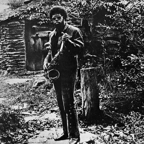 Black and white portrait of Joe McPhee with a saxophone, outdoors.