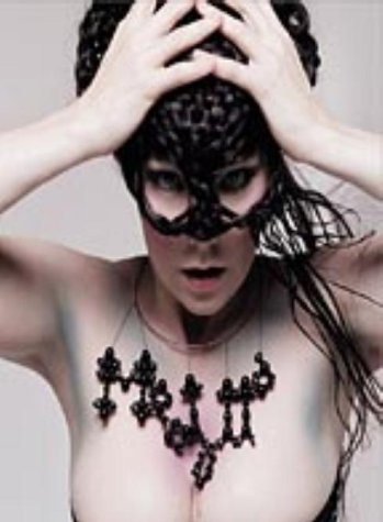 Björk wearing a black lattice headpiece and a matching beaded necklace against a background.