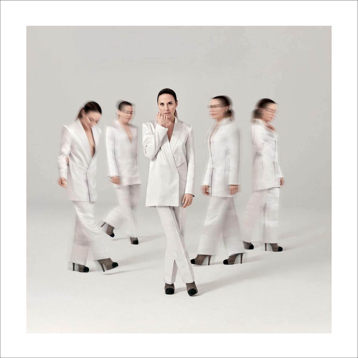 Melanie C in white suit, surrounded by blurred duplicates, against a plain white background.