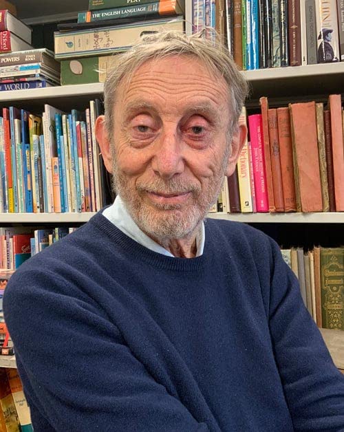 Michael Rosen, author of "Oww!", smiles in front of bookshelves.
