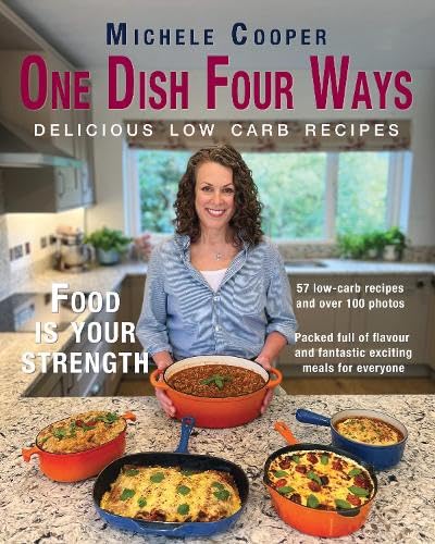 A woman stands in a kitchen behind four colorful pans of prepared food.