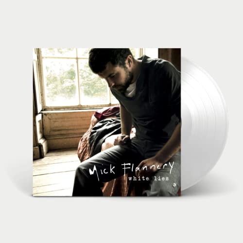 Mick Flannery sitting on a bed by a window, with a white vinyl record.