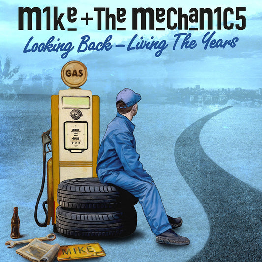 A mechanic sits on tires next to a gas pump overlooking a distant city.