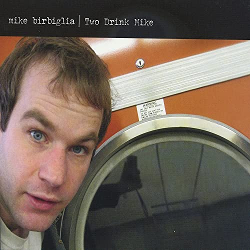 Mike Birbiglia posing next to a round orange laundry dryer door.