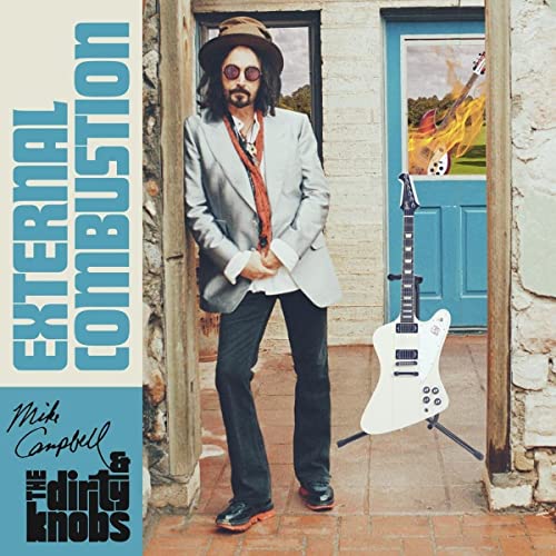 Mike Campbell stands in a doorway next to a white electric guitar on a stand.