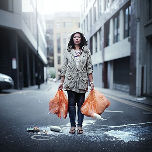 Woman with shopping bags stands in a city street with spilled groceries.