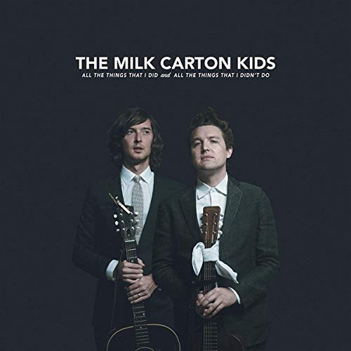 Two men in suits holding guitars on a dark album cover.