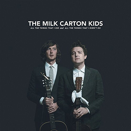 "Album cover featuring two men in suits holding guitars against a dark background."