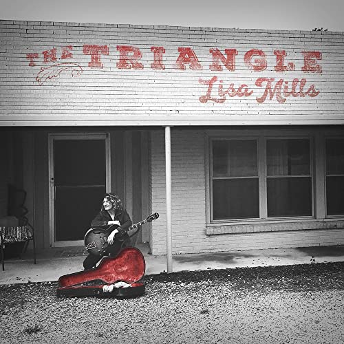 Woman sitting outside building with guitar, case beside her, on gravel ground.