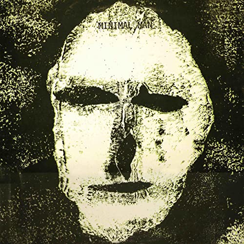 Pale, textured mask face on a dark, grainy background.