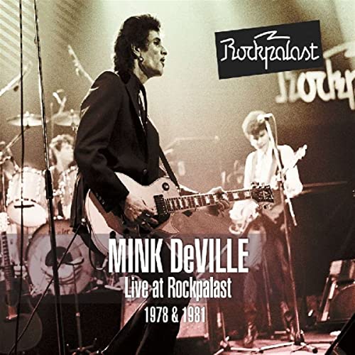 Mink DeVille performing live on stage with guitars and drums.