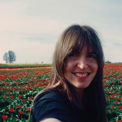 Woman with brown hair smiles in a field of red tulips.