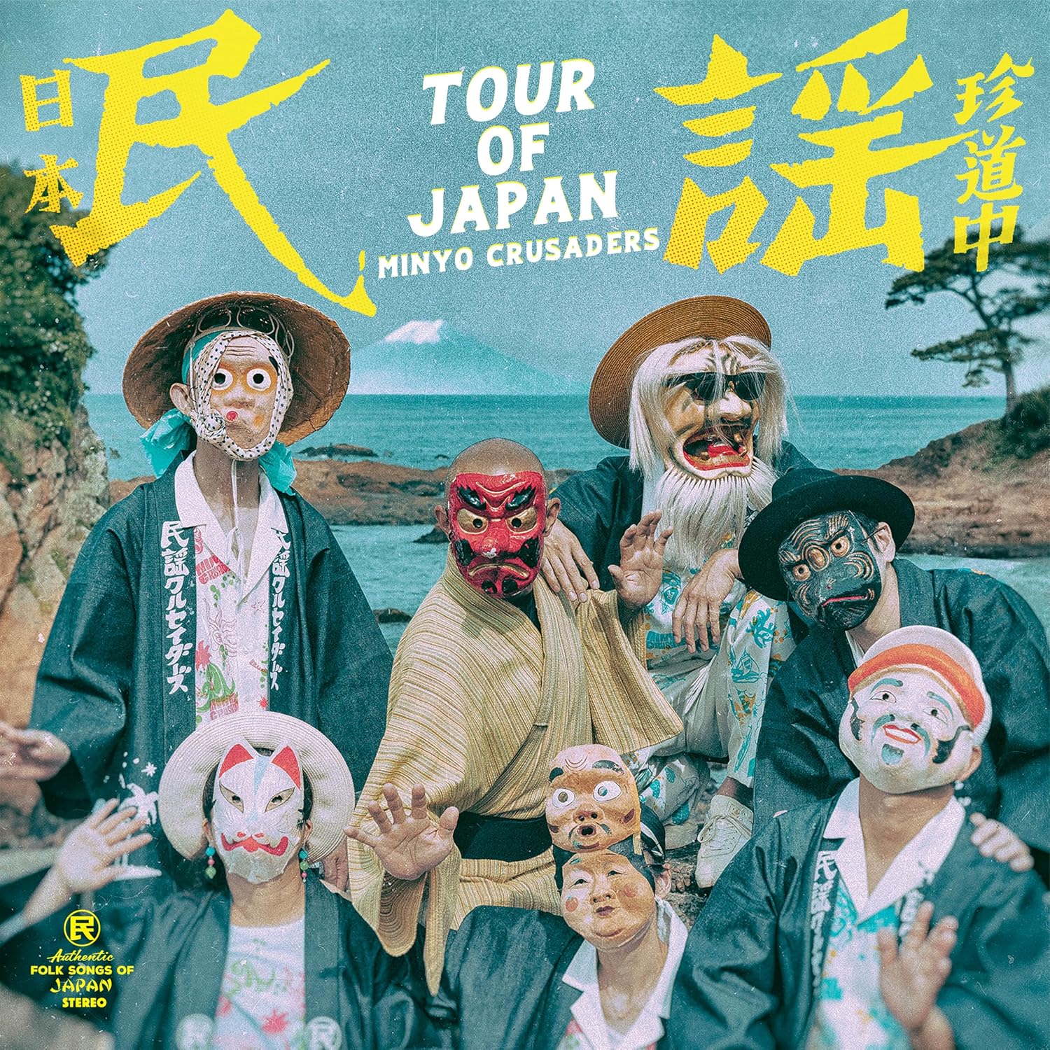 Seven people wearing traditional Japanese masks and clothing pose before a coastal landscape.