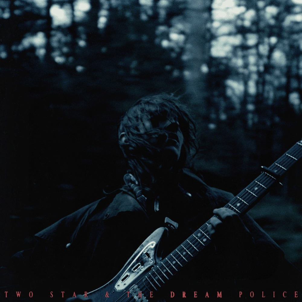A person with messy hair plays an electric guitar in a dark, moody forest setting.