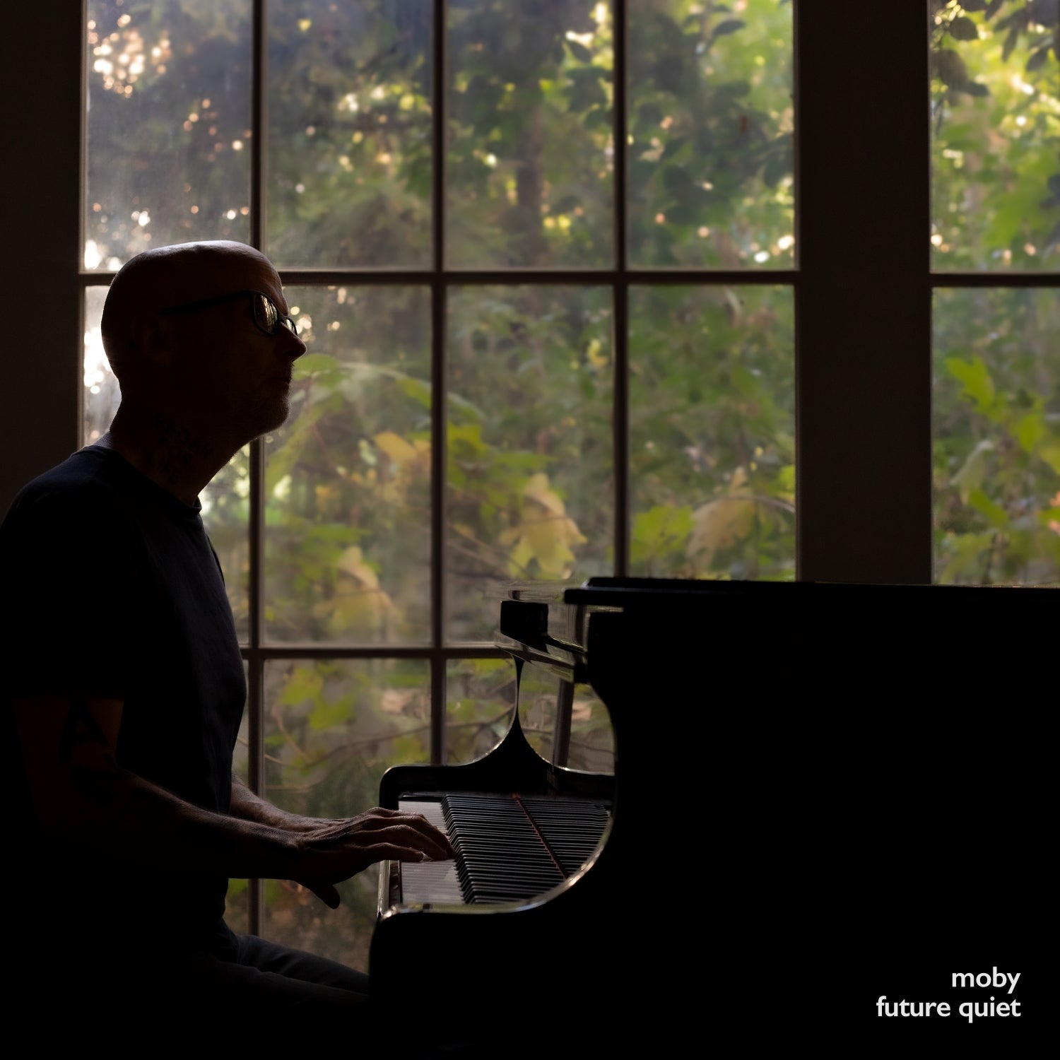 Silhouetted man playing a piano in front of a window.