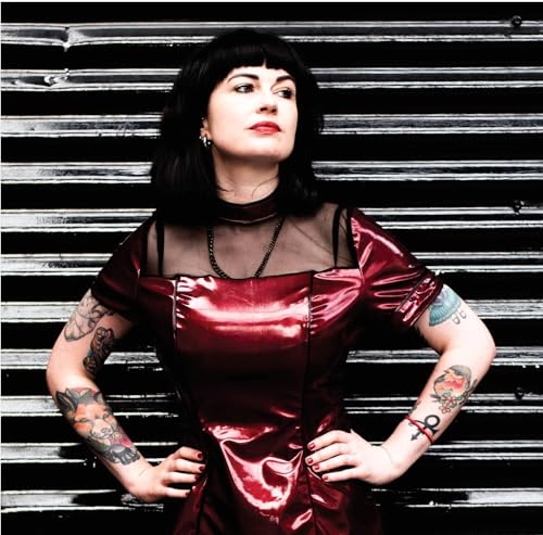 Woman with dark hair and tattoos poses in front of striped metal.
