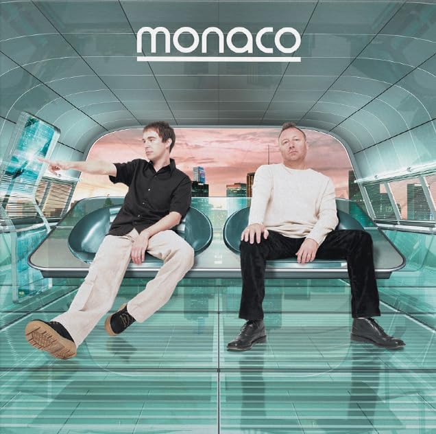 Two men sitting in a futuristic, glass-walled room with a city skyline in view.