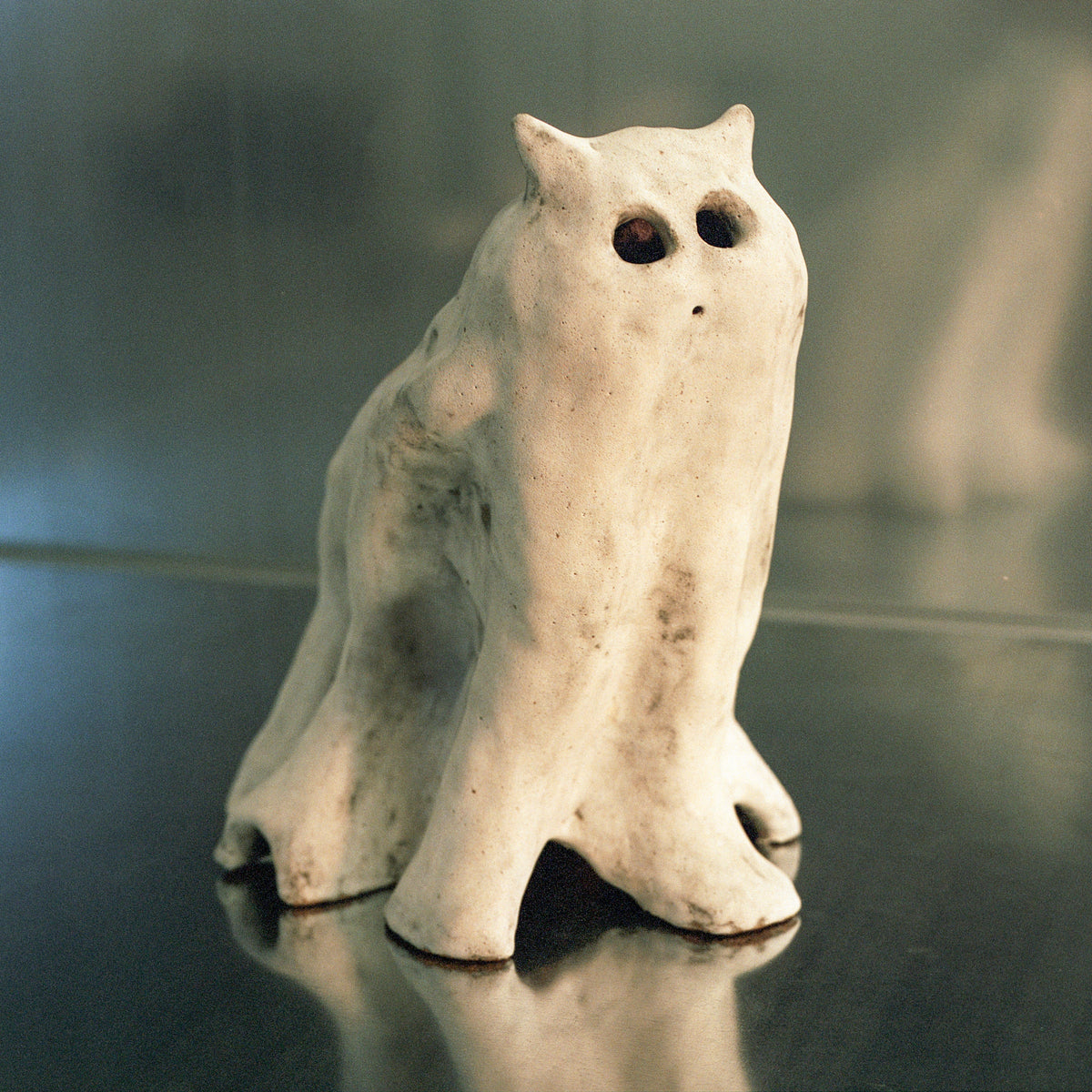 White, textured ceramic sculpture of an animal-like figure on a dark surface.