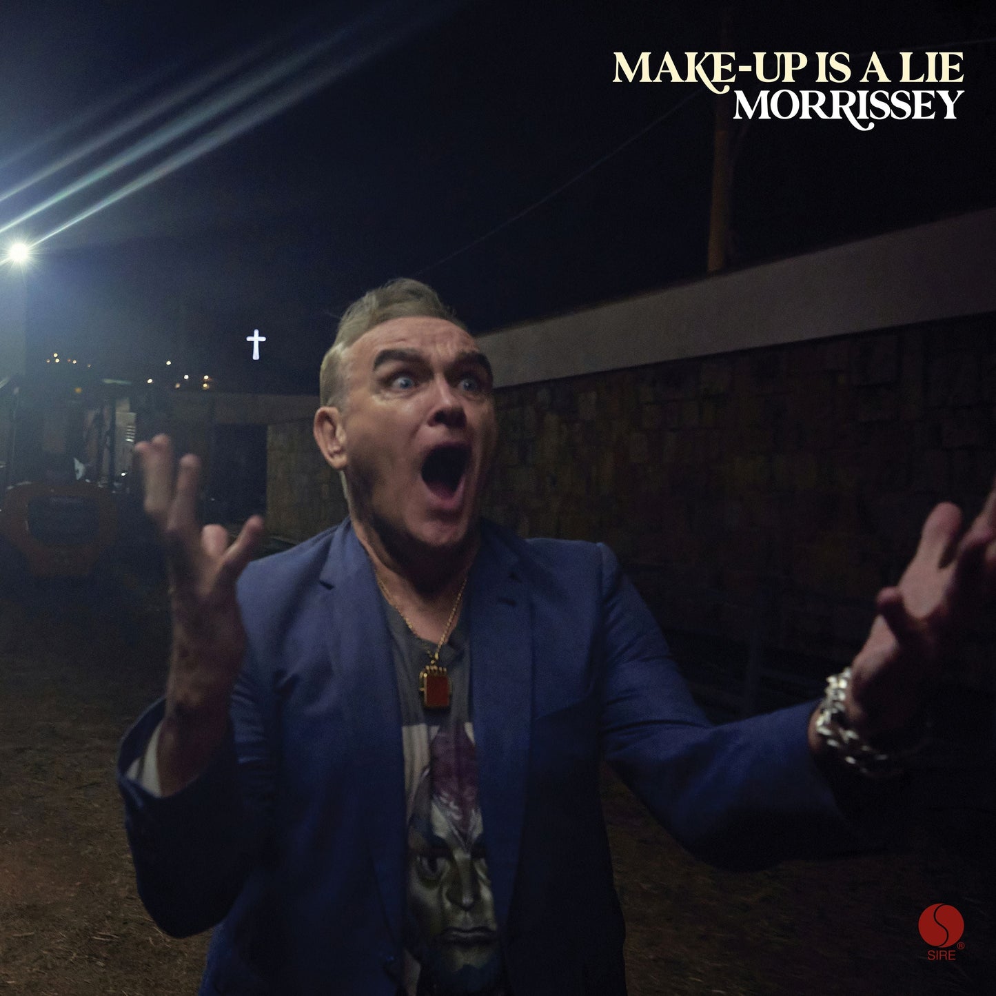 Morrissey with mouth open and hands raised in a dark outdoor setting at night.