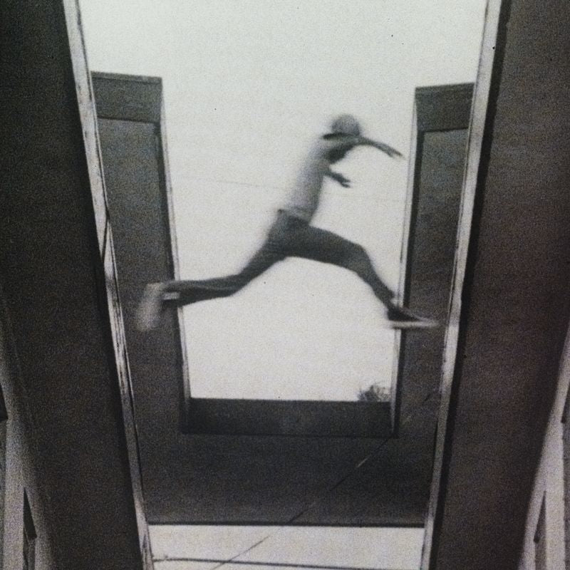A blurry black and white photo of a person jumping between two tall structures.
