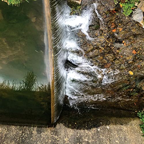 Water flows over a straight concrete edge into a rocky stream below.