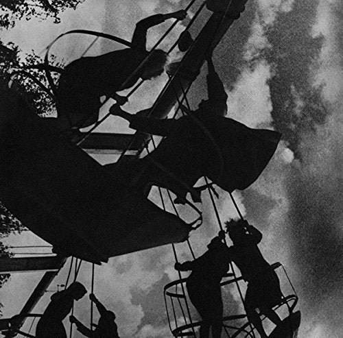 "Black and white image of silhouetted people on a spinning carnival ride against a cloudy sky."