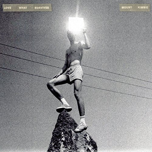 Black and white album cover featuring a person atop a rock with a bright light.