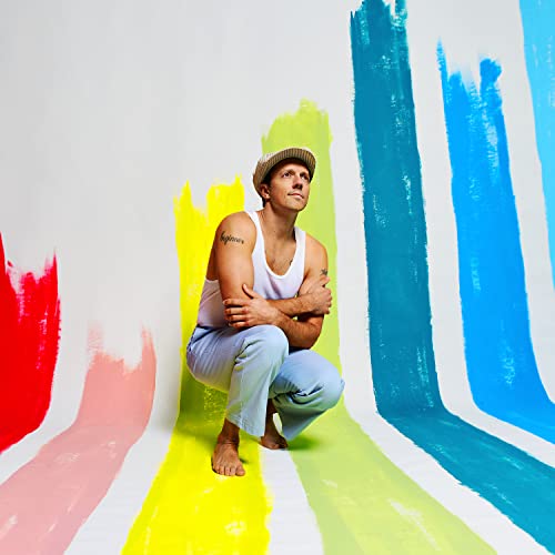 Jason Mraz squats against a wall with colorful painted brushstrokes.