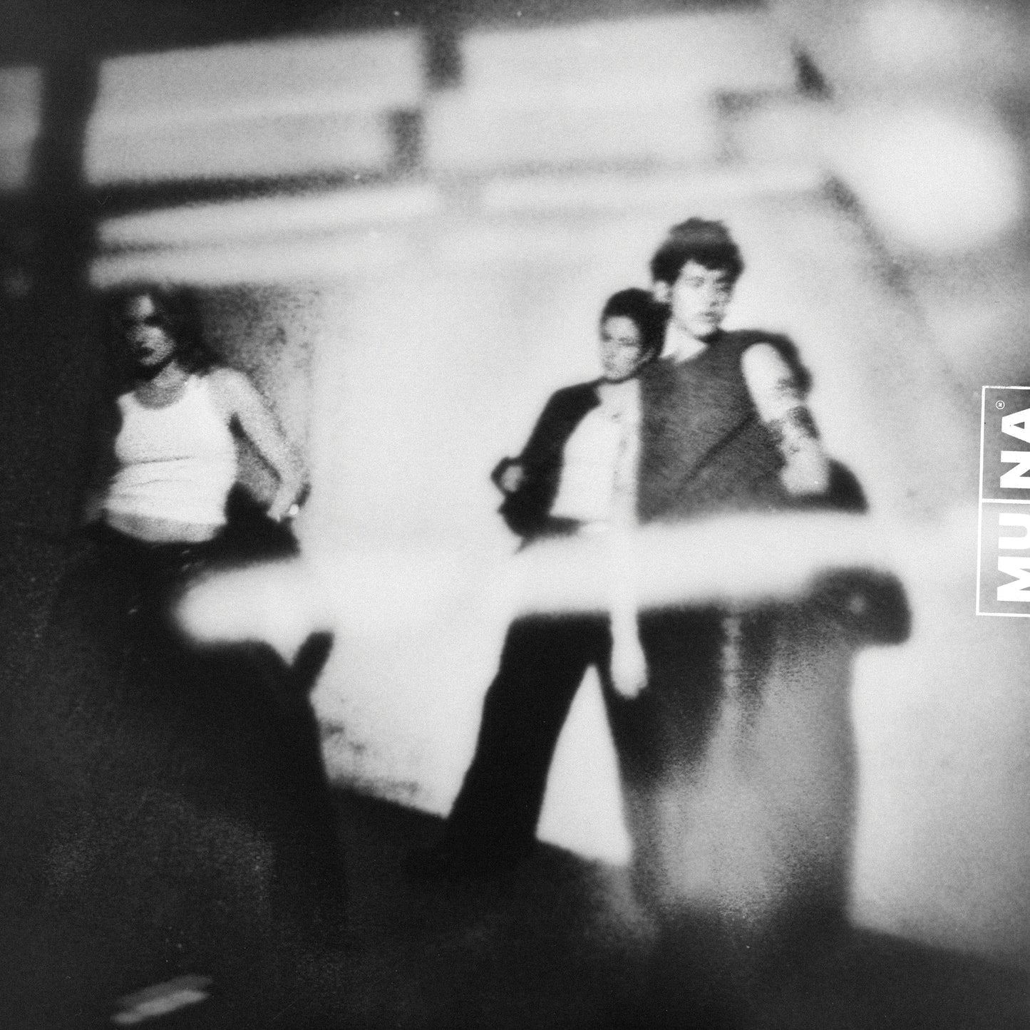 Blurred black and white photo of three people against a wall.