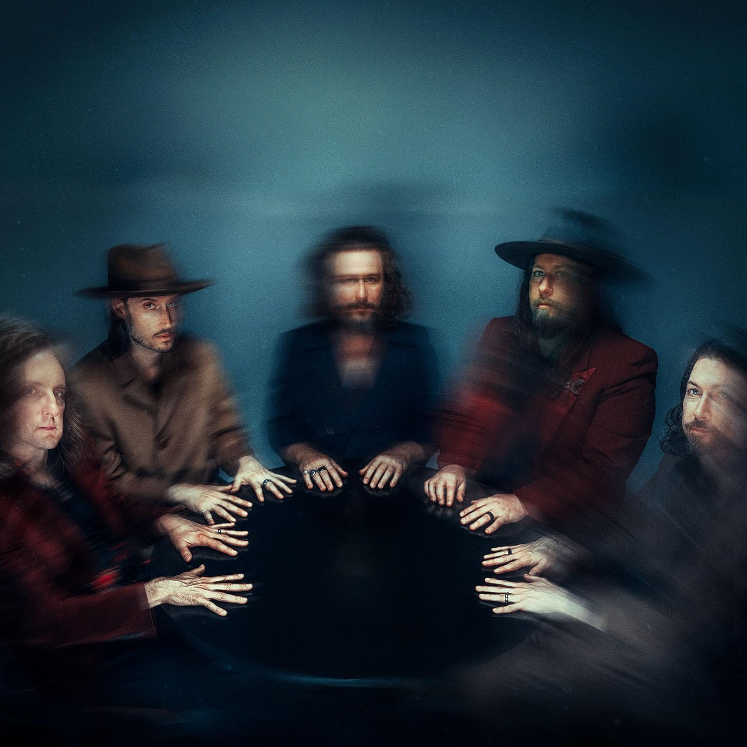 Five band members sit around a circular table in a moody, motion-blurred portrait.