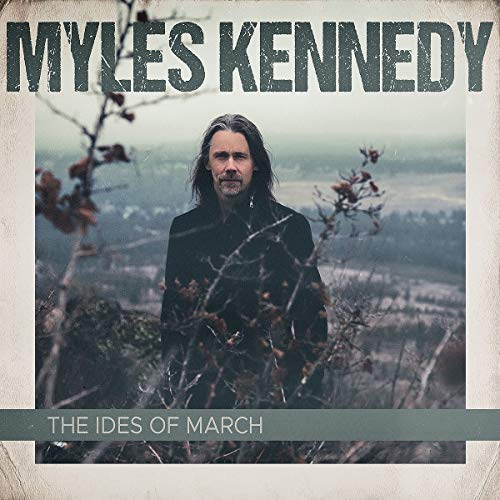 Myles Kennedy stands in a field behind bare branches on this album cover.