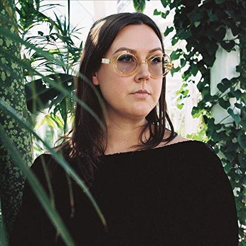 Nadia Reid portrait, wearing large yellow-tinted glasses, surrounded by greenery.