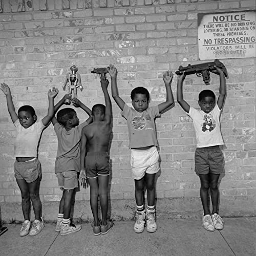 Black and white photo of young boys raising objects against a brick wall.