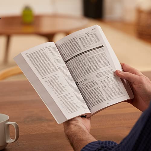 Open hardcover Bible with text, held by a person’s hands.