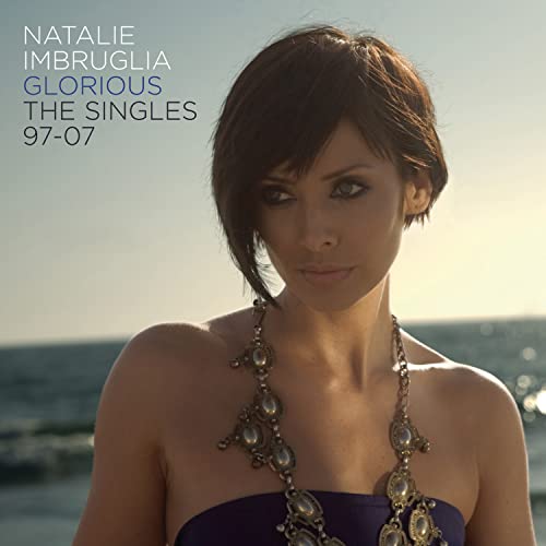 Natalie Imbruglia wearing a necklace against a beach background with album title text overlay.