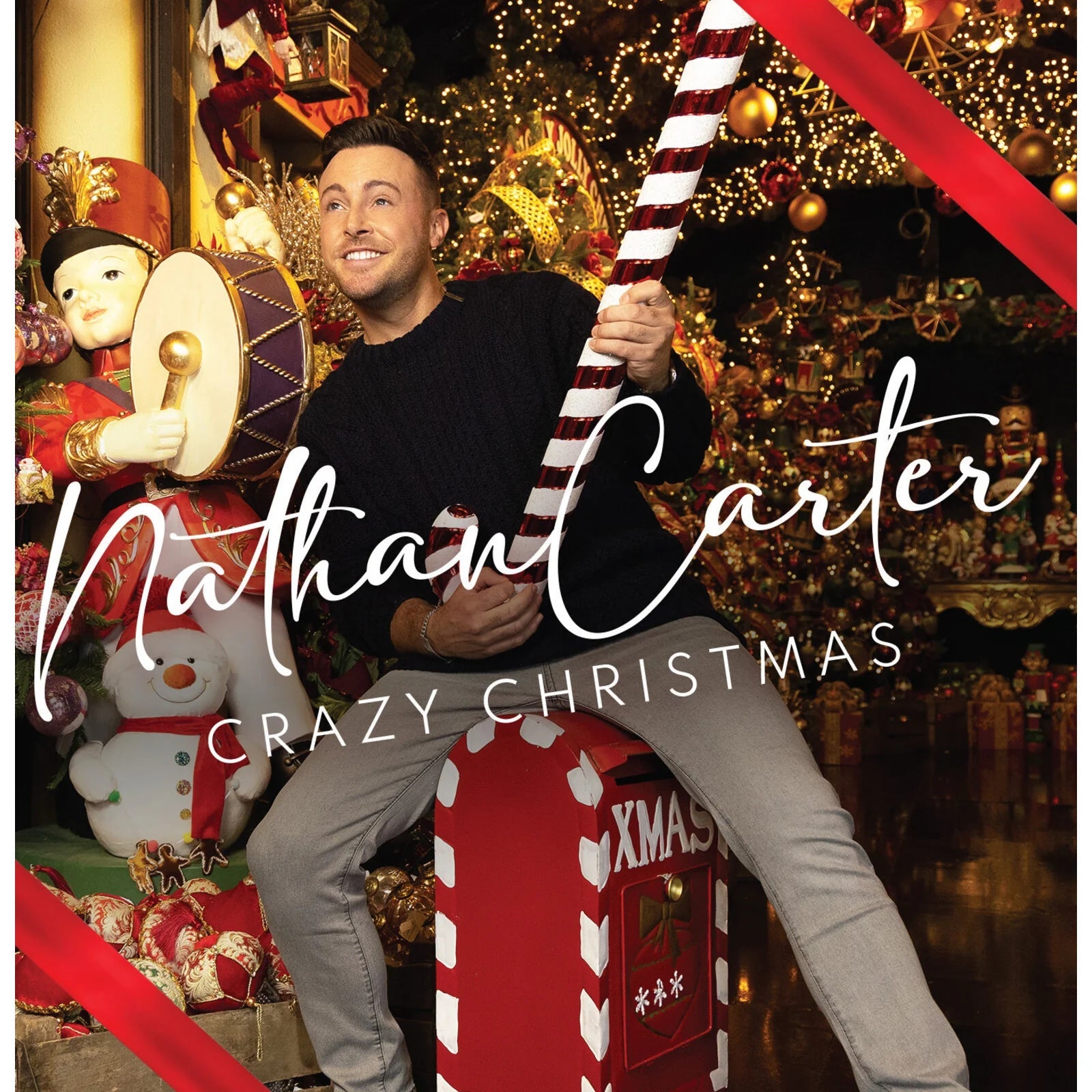 Man in black sweater holding a giant candy cane amidst festive Christmas decorations.