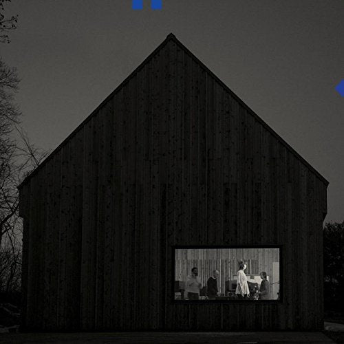 The image depicts a dark wooden barn with a band visible through a window. The alt text is: "Dark barn with band visible through a rectangular window."