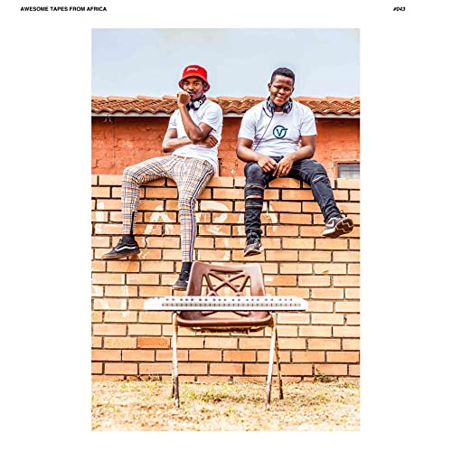Two young men sitting on a brick wall behind a keyboard on a chair.