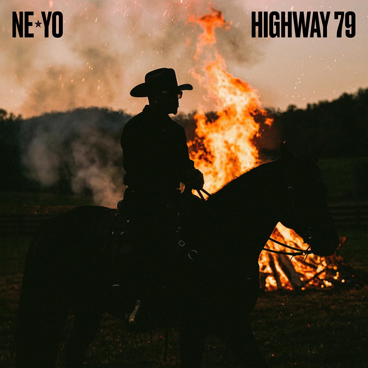 Silhouette of a cowboy on horseback in front of a large fire at sunset.