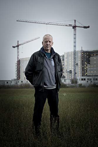 Man standing in a field with construction cranes and buildings behind him.