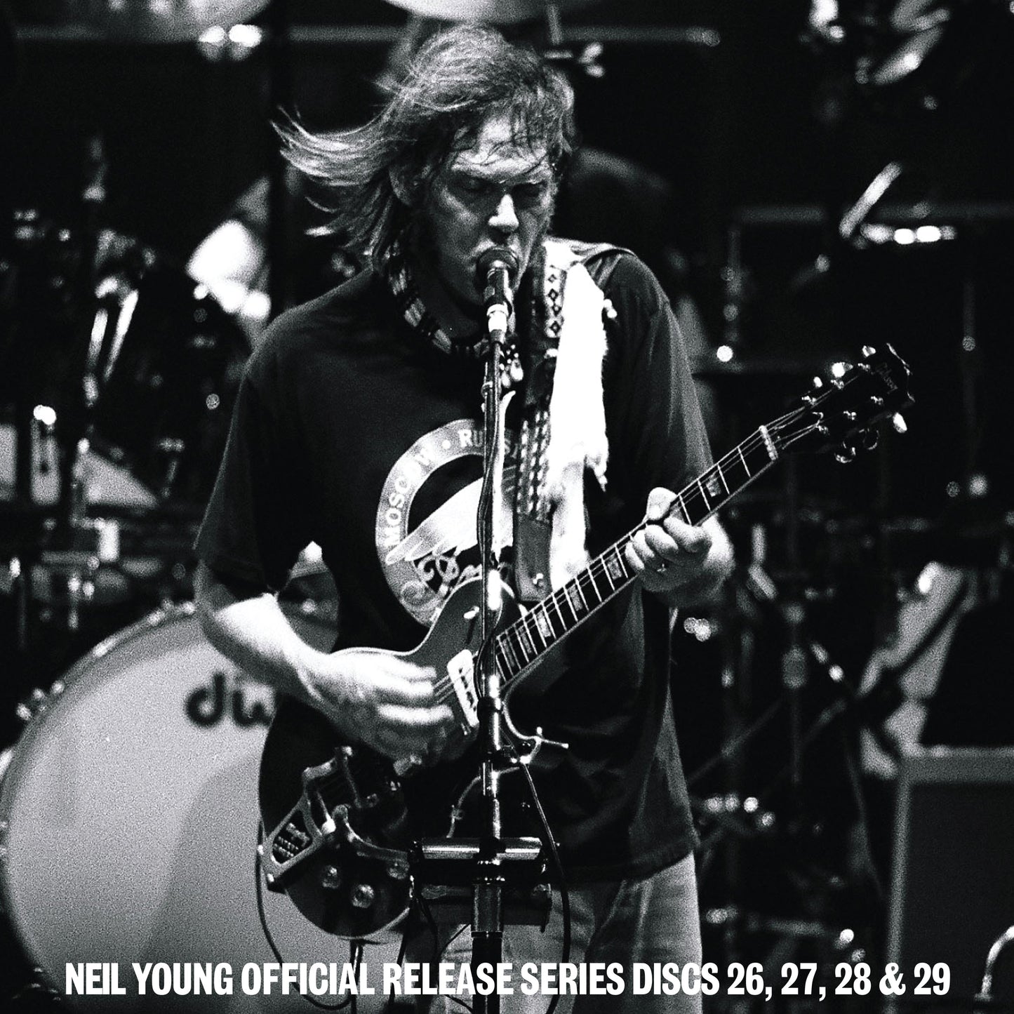 Black and white photo of Neil Young performing on stage with his electric guitar.
