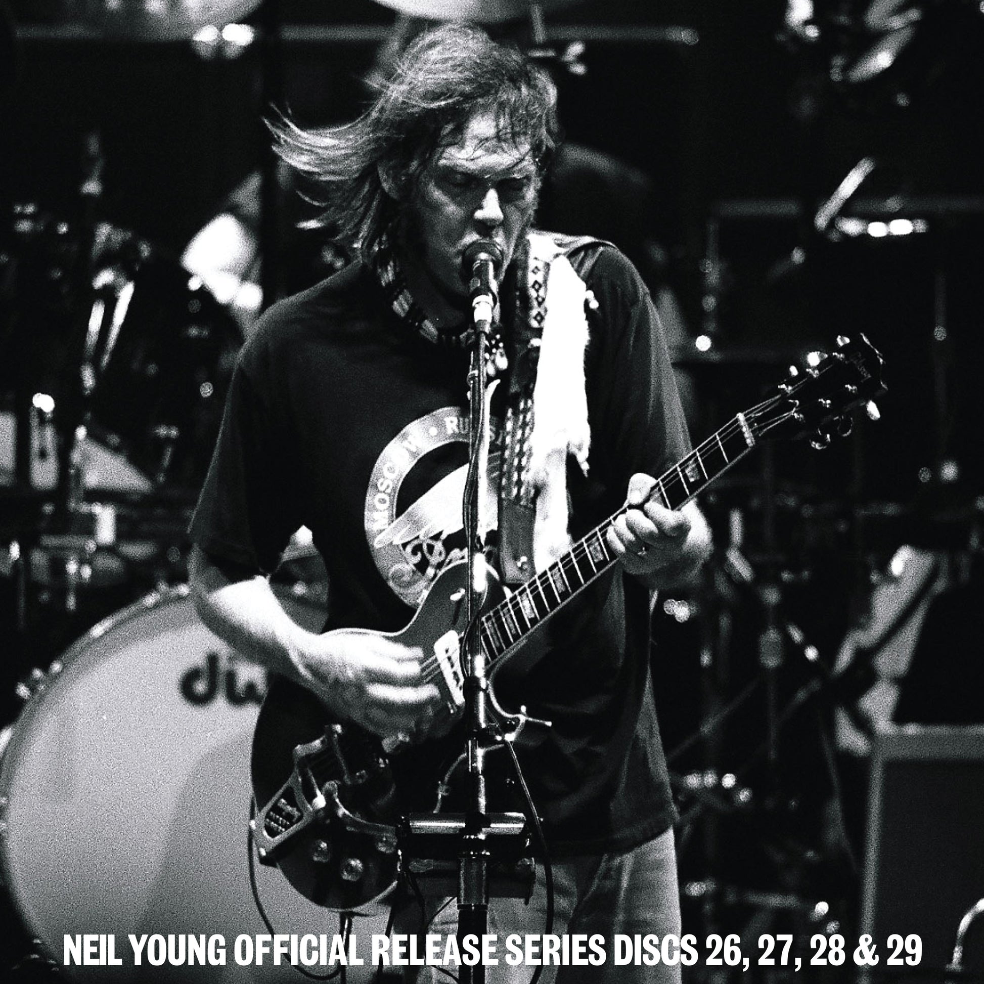 Black and white photo of Neil Young performing on stage with his electric guitar.