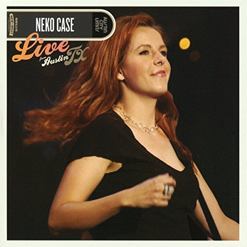 Neko Case with long red hair performing on stage against a dark background.