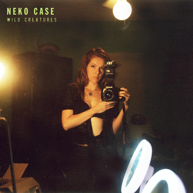 Neko Case album cover: woman with vintage camera, dark background.