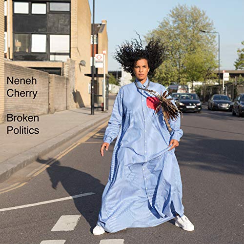 Neneh Cherry stands on a street wearing a long blue striped dress.