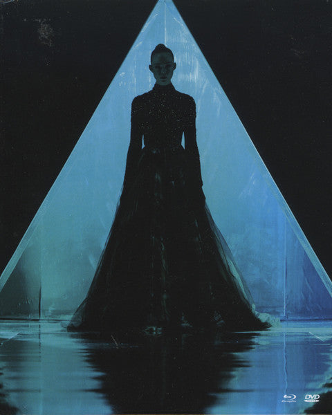Woman in black gown stands in a bright, triangular light.