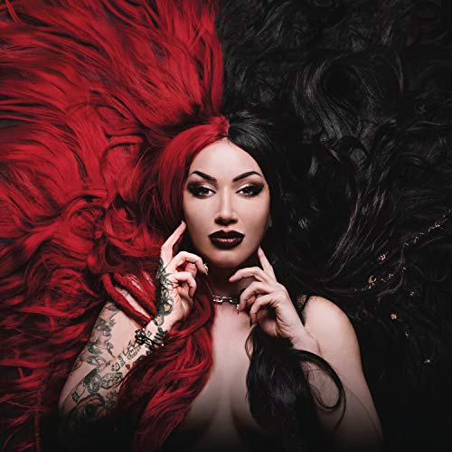 Woman with red and black hair, tattoos, and feathered attire posing for a music album cover.