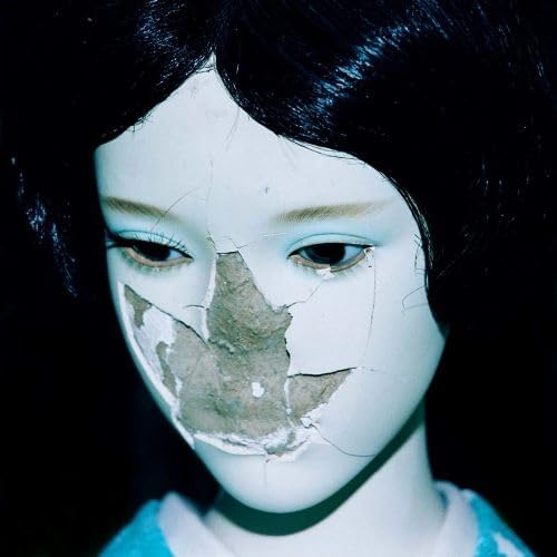 Close-up of a pale face with cracked porcelain skin and dark hair.